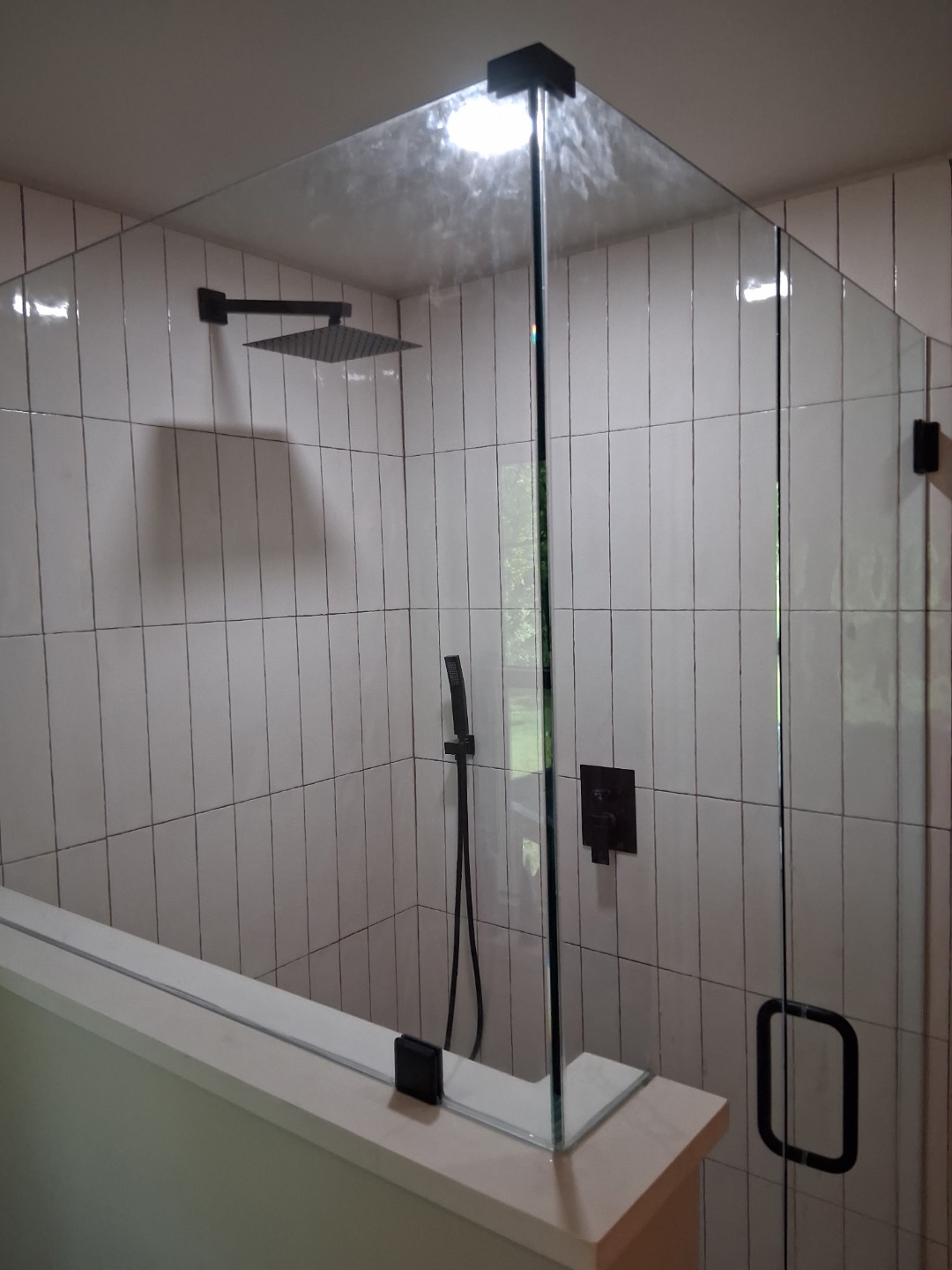 Frameless glass shower enclosure with rain head and hand wand, white vertical tile